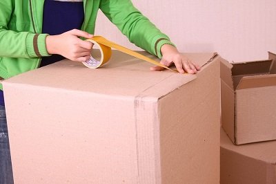 A lady using masking tape on a box for moving house.